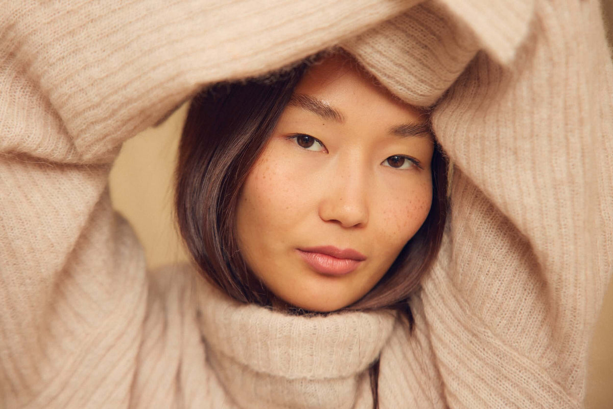 Close-up of a woman in a cozy beige sweater, showcasing her natural beauty and serene expression.