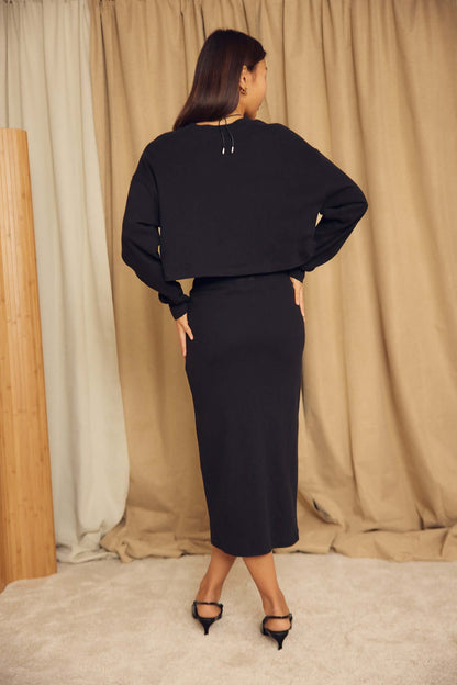 Black Organic Cotton Pencil Midi Skirt shown on model from the back, showcasing the minimalist design and elegant fit.