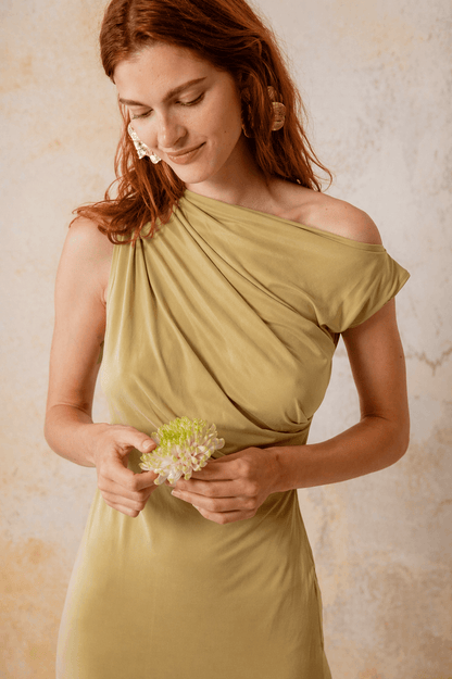 Drape Cupro Midi Dress in Olive worn by a model holding a flower, showcasing its elegant draped neckline.