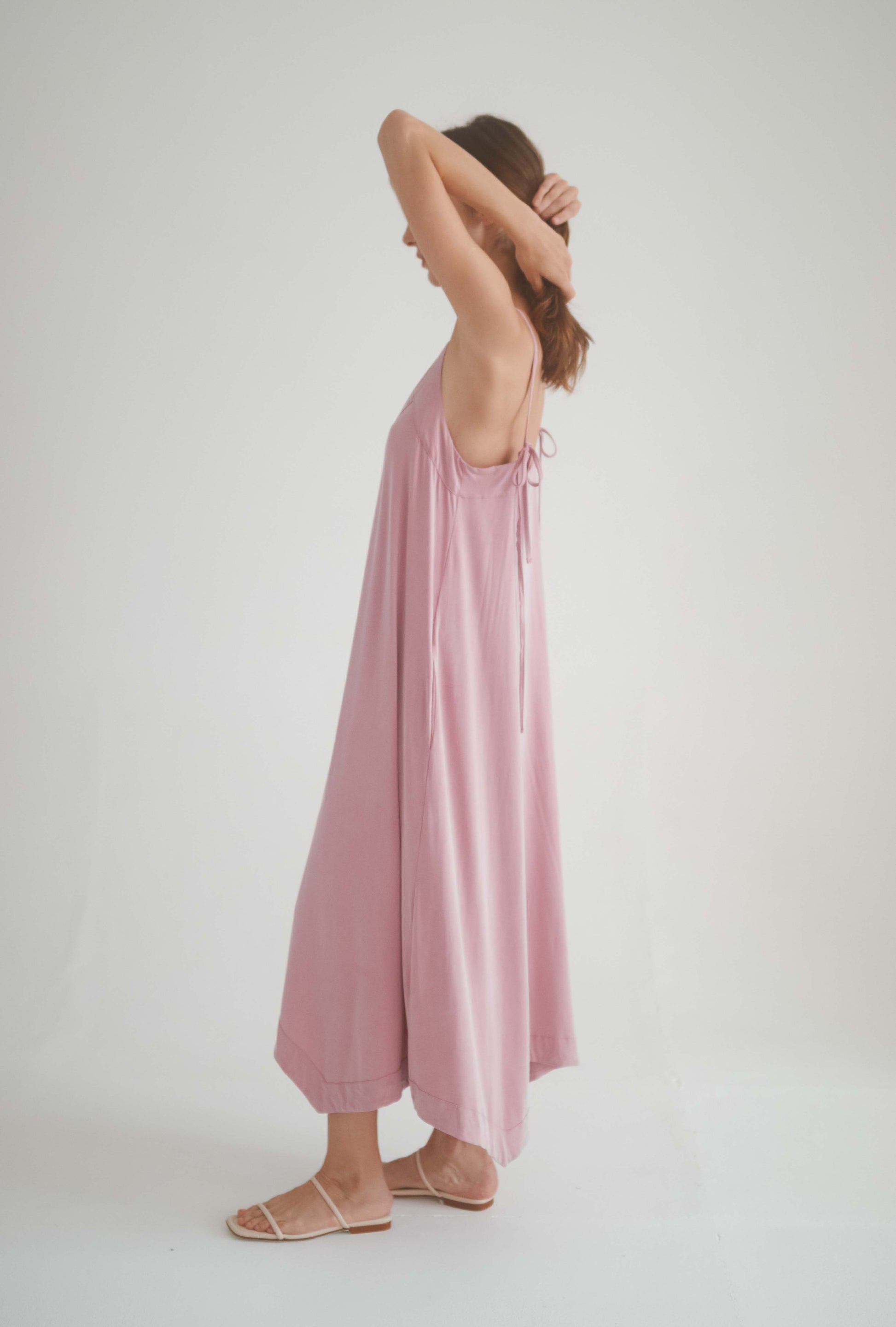 Model wearing ROSE CUPRO MIDI DRESS in blush pink, showcasing adjustable self-tie straps and flowy design.