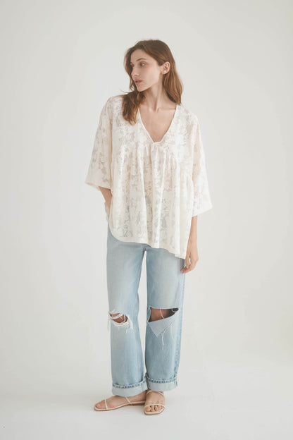 Model wearing a lace boho tunic top with a V-neckline and wide sleeves, paired with ripped jeans.