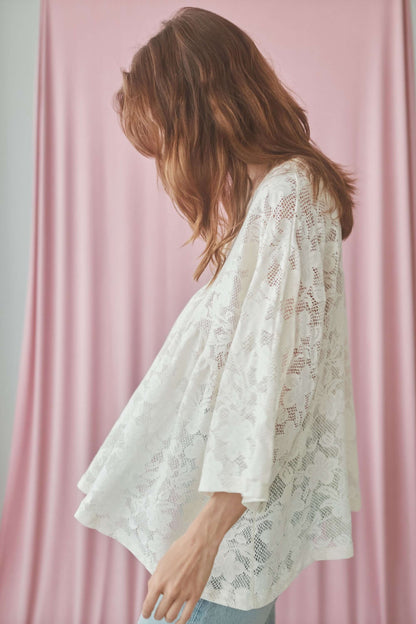 Model wearing a lace boho tunic top with V-neckline and wide sleeves, set against a pink backdrop.