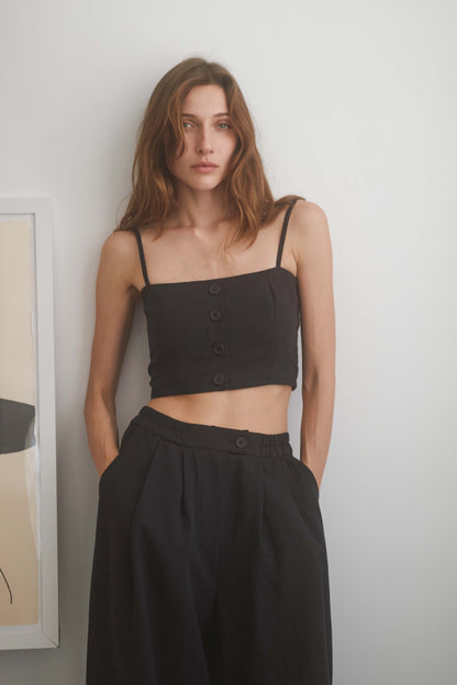 Model wearing a black crop top with eco buttons and adjustable straps, paired with wide trousers.