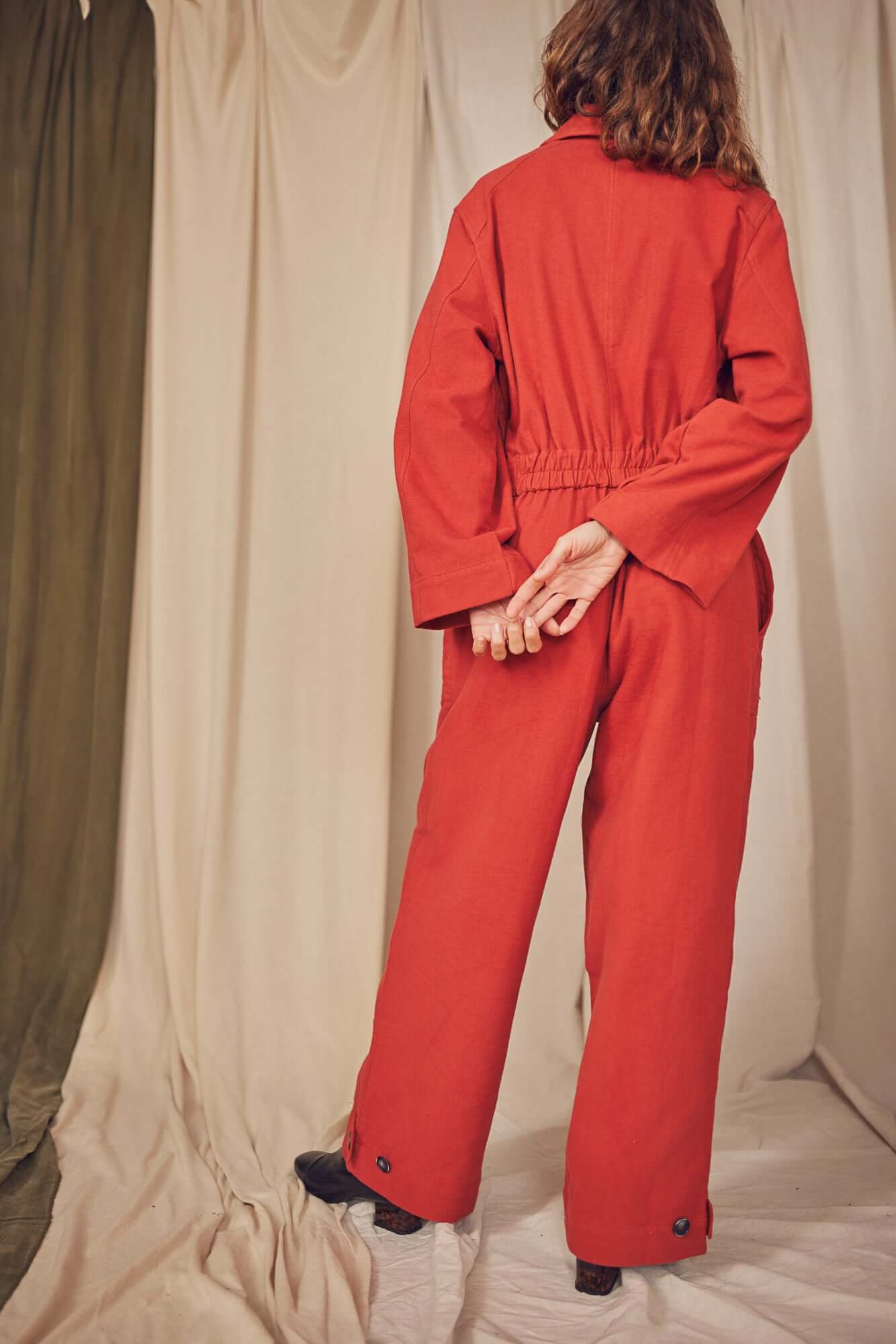 Model wearing a Rust Organic Cotton Boiler Suit, showcasing the back with a flattering waist detail and eco-friendly buttons.