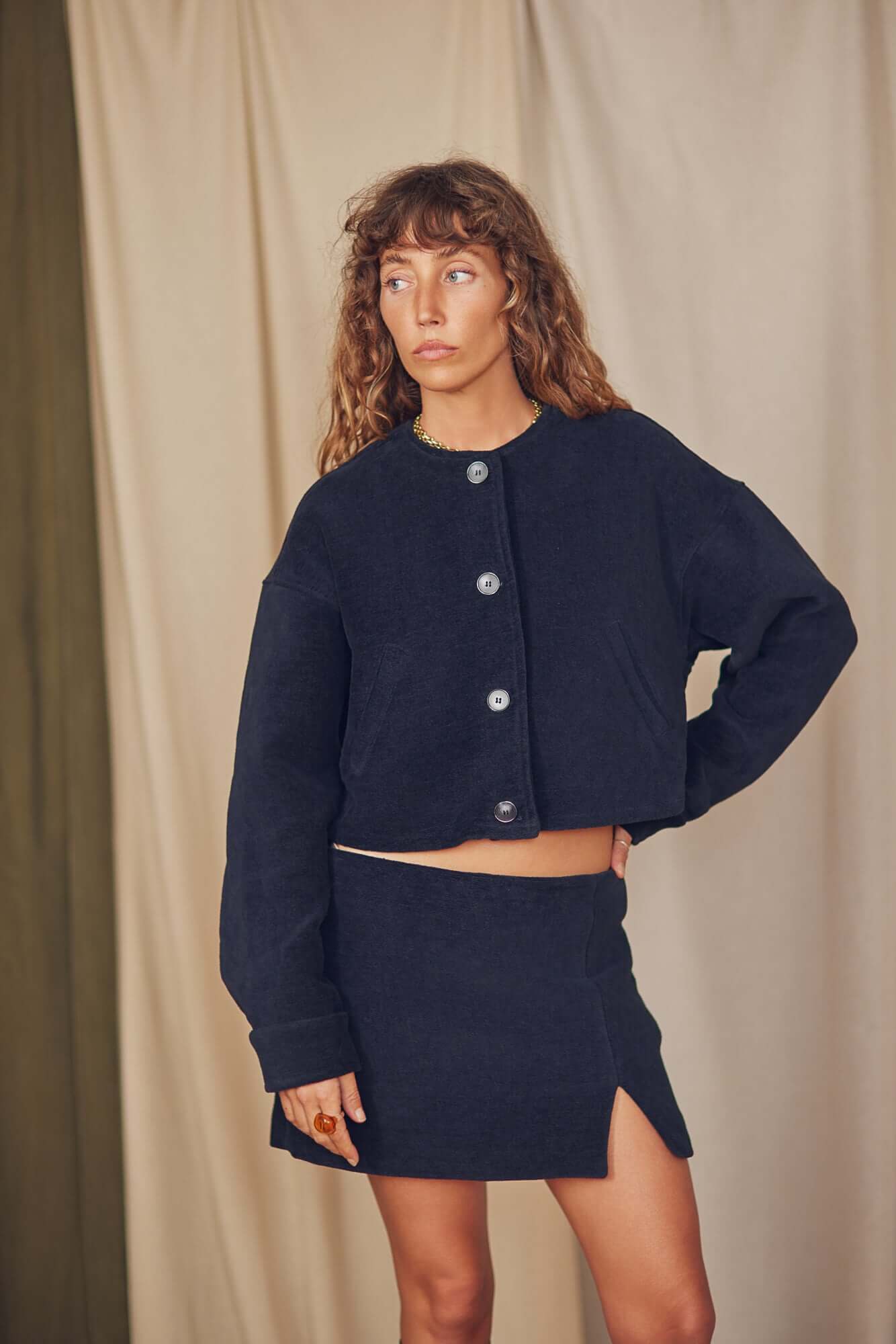 Model wearing a black organic cotton mini skirt with a matching cropped jacket, showcasing a chic autumn look.