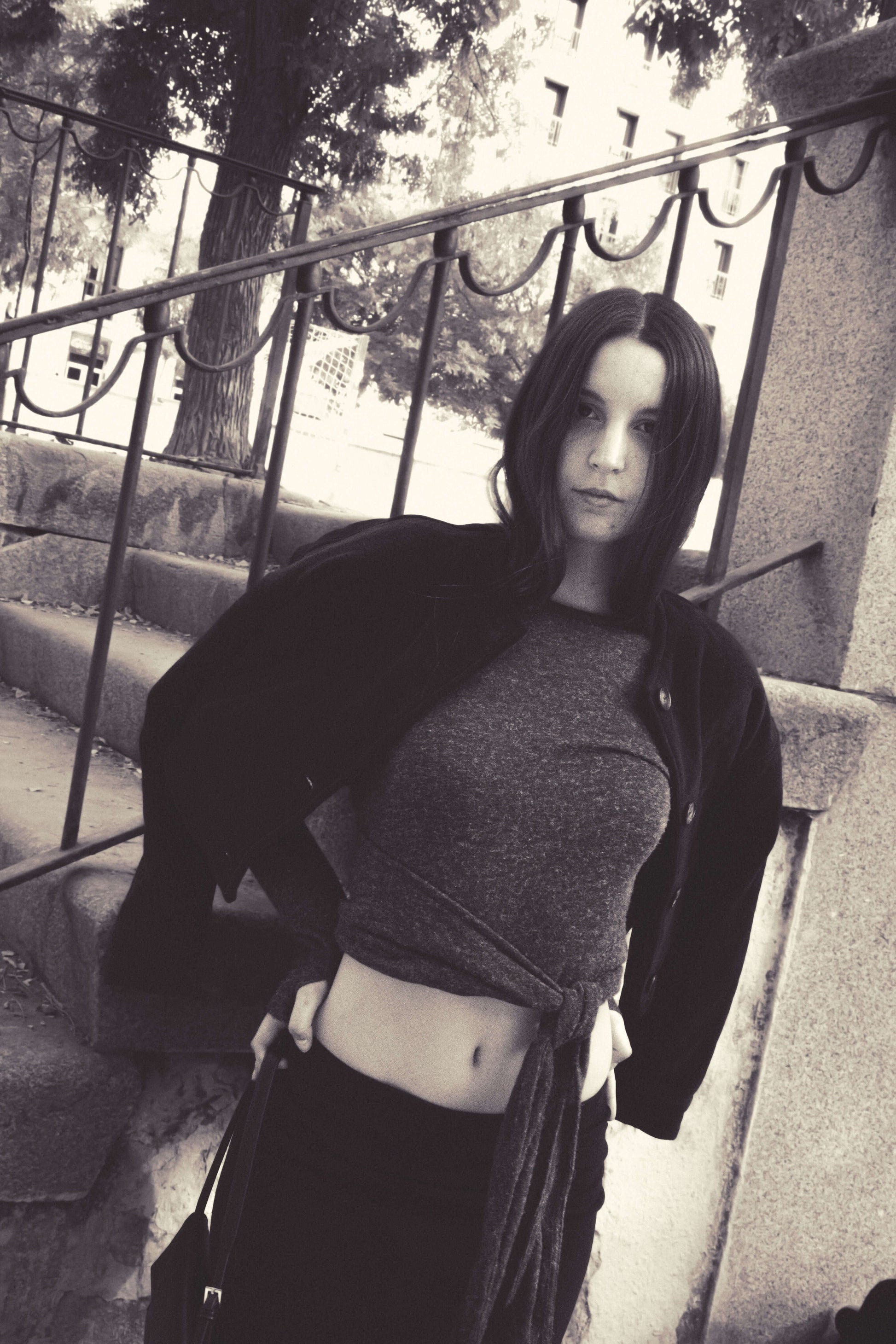 Fashionable woman in casual outfit with a tied grey top and black jacket, posing outdoors