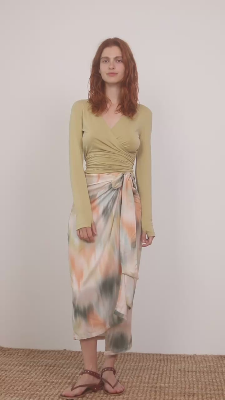 Cupro Multiway Wrap Top in Soft Olive worn with a vibrant tie-dye skirt, showcasing versatile styling options.